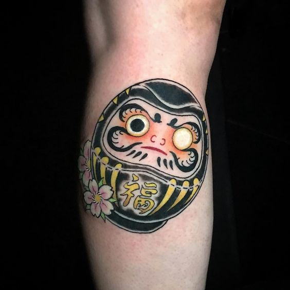 kiểu xăm hình daruma mặt tròn màu đen có hoa anh đào làm điểm nhấn